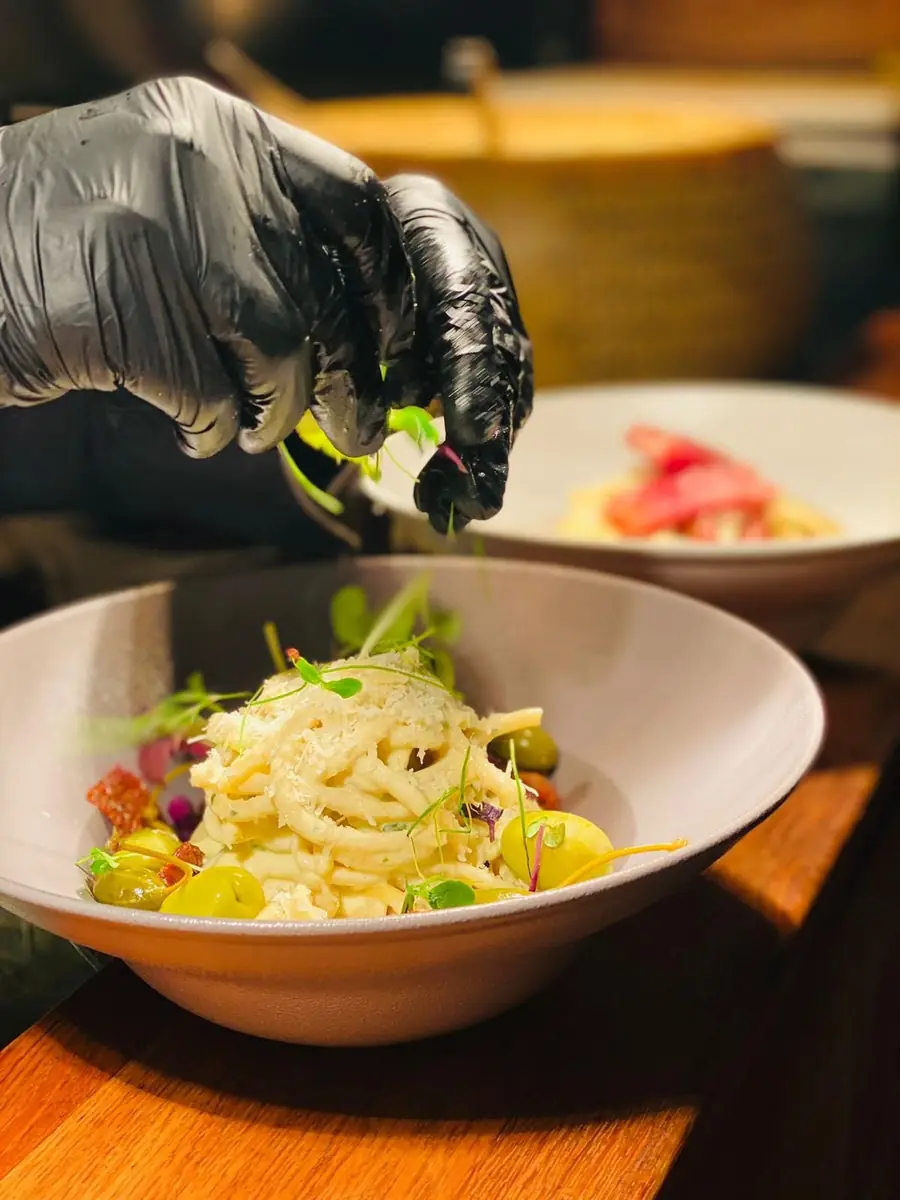 Koch verfeinert Spaghetti mit Kräutern und Parmesan